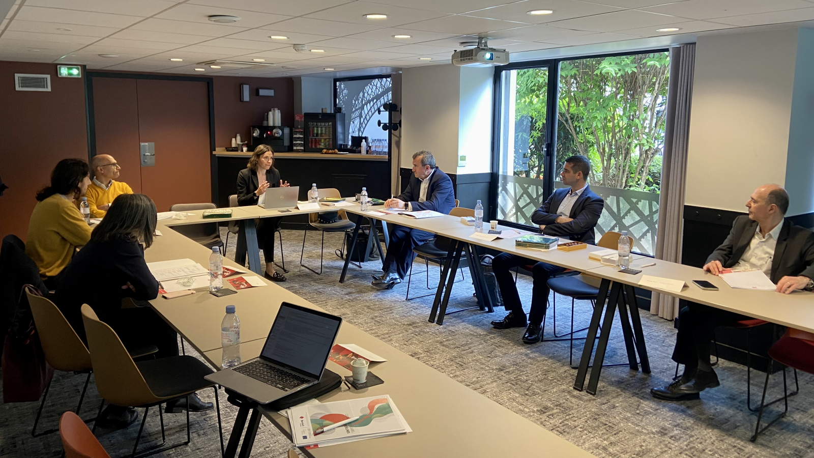 Seven people are seated around a U-shaped meeting table.