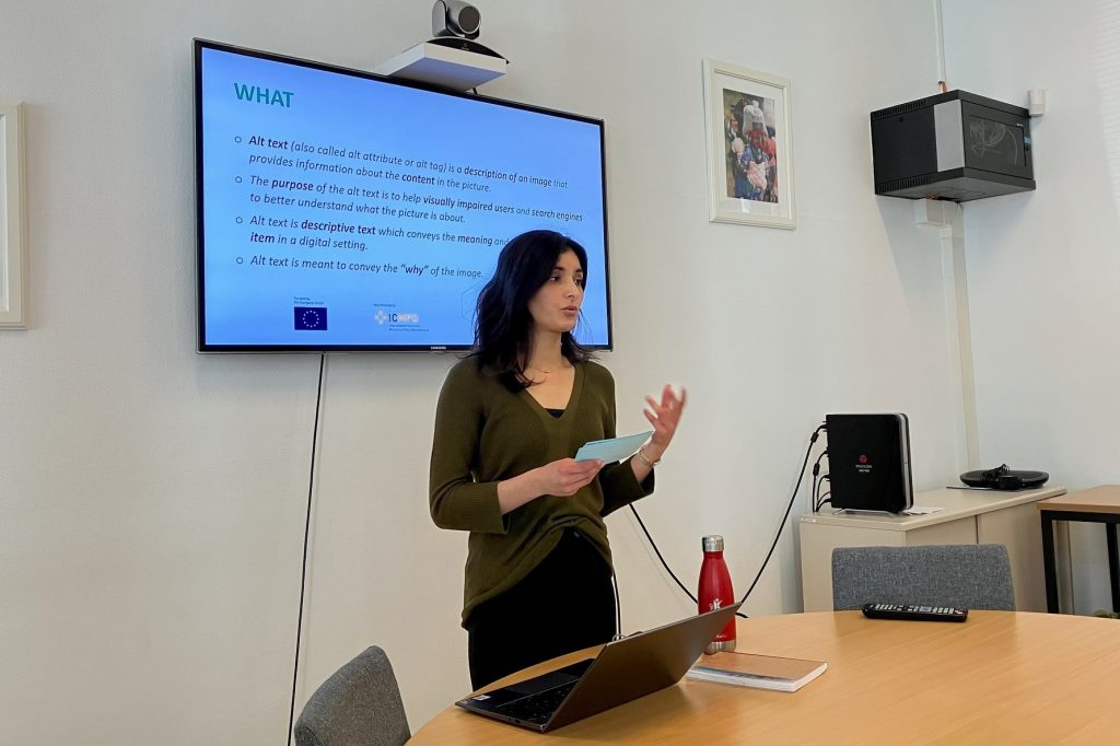 A young woman standing in front of a screen giving a presentation about writing alt-text.