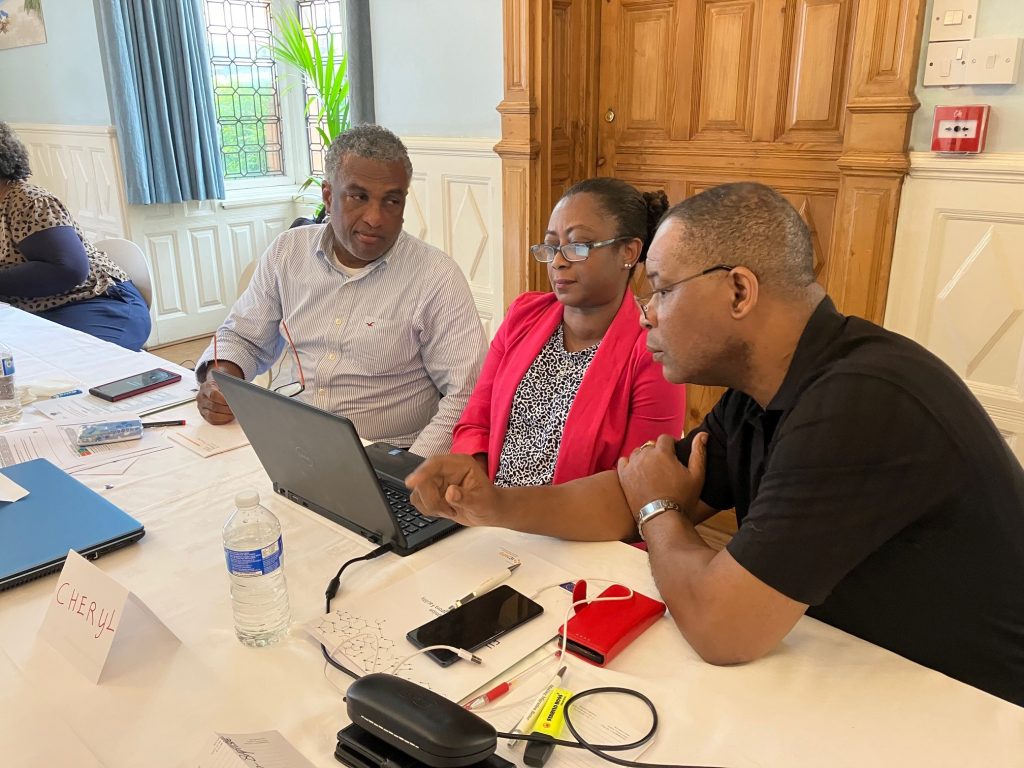 A woman and two men are looking together at a laptop.