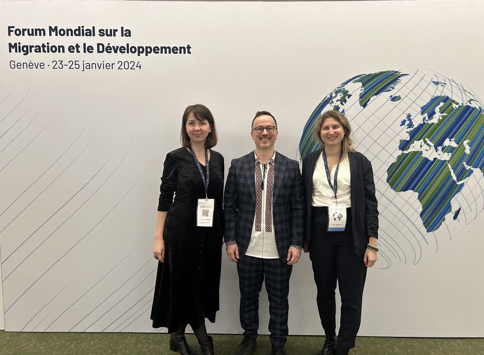 Two women and a man stand in front of a sign for the Global Forum on Migration and Development, smiling at the camera.