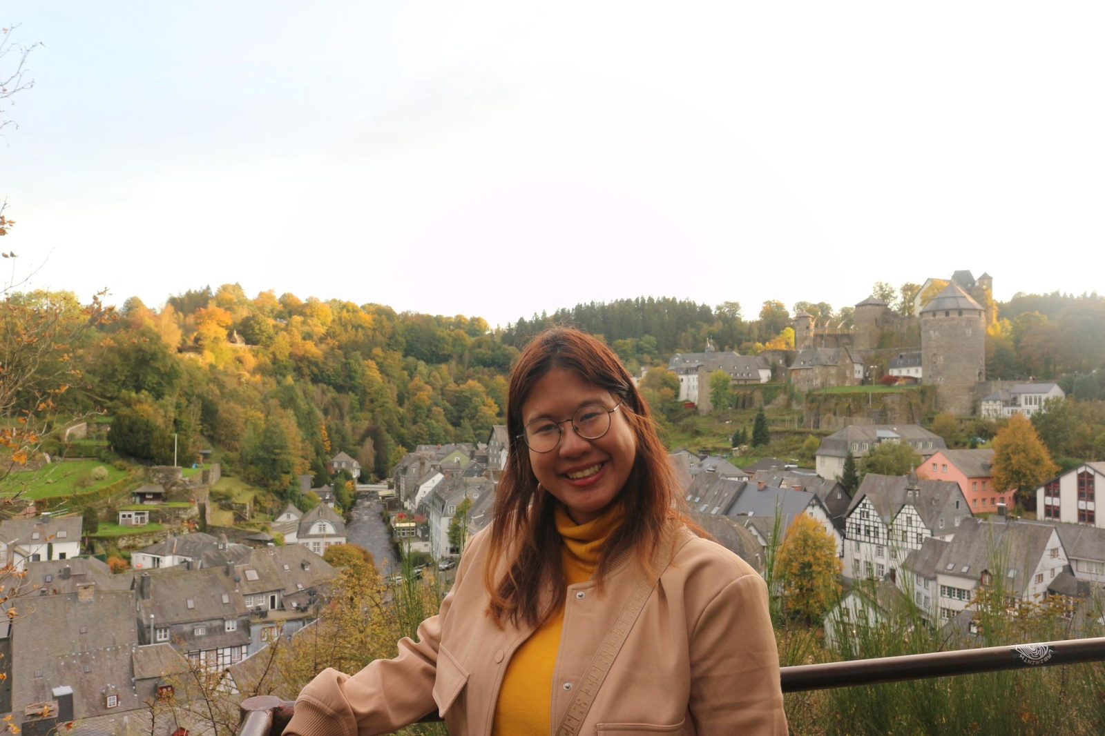 Nicha, a young woman standing in front of a panoramic view of old town Monschau, Germany